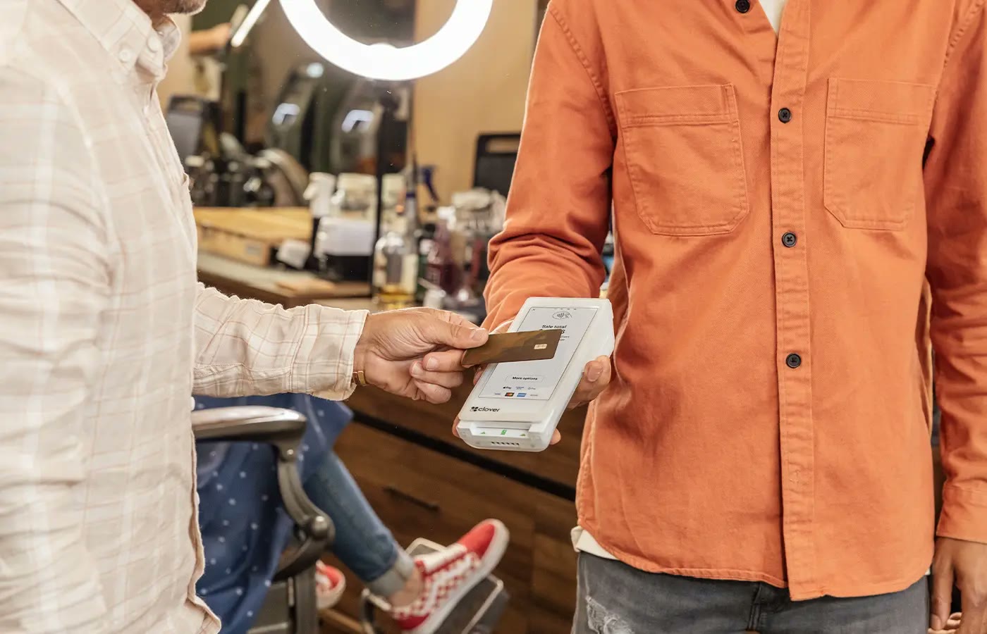 A customer hands a card to a barber holding a Clover Flex handheld terminal at the counter.