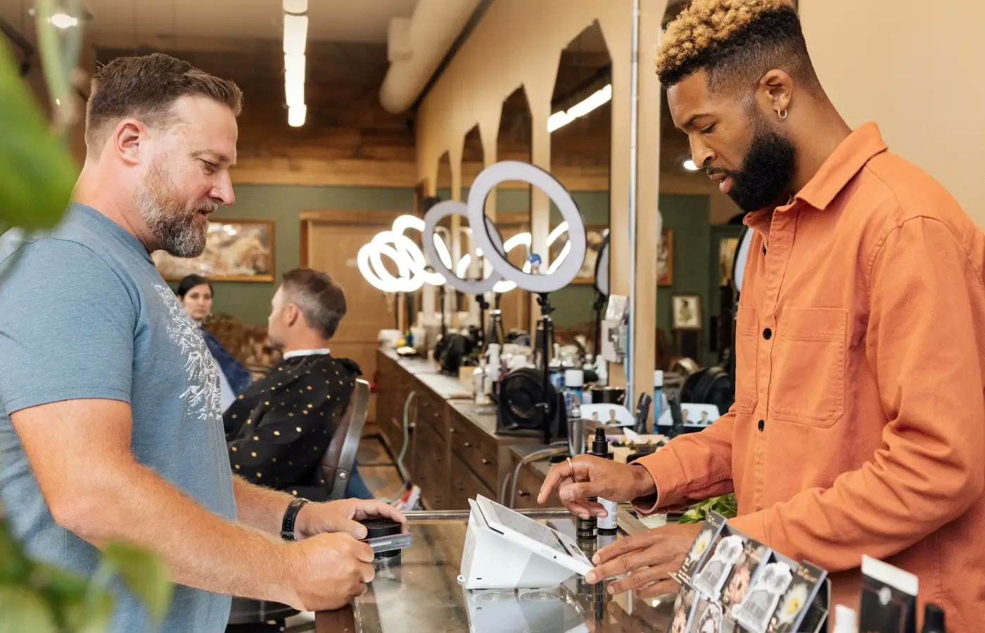 Barbershop owner ringing up a customer at a counter-mounted register.