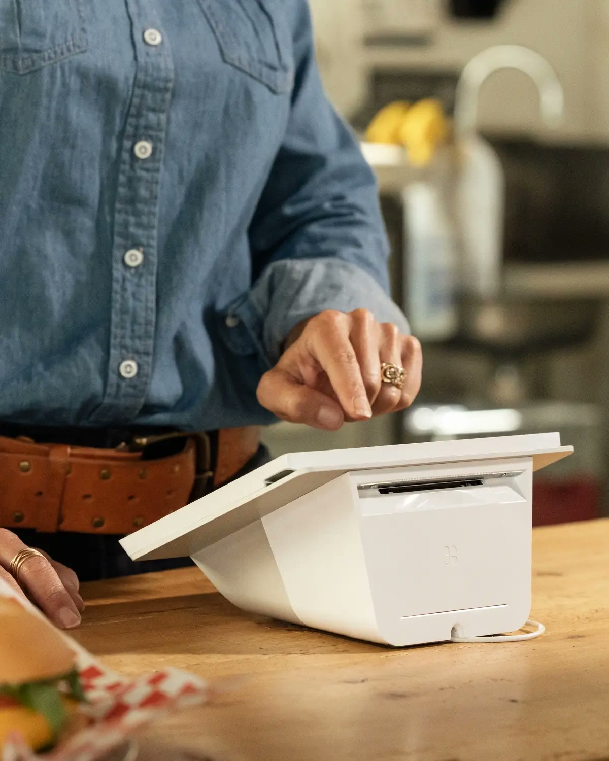 Close-up of a compact countertop terminal printing a receipt beside a sandwich order.