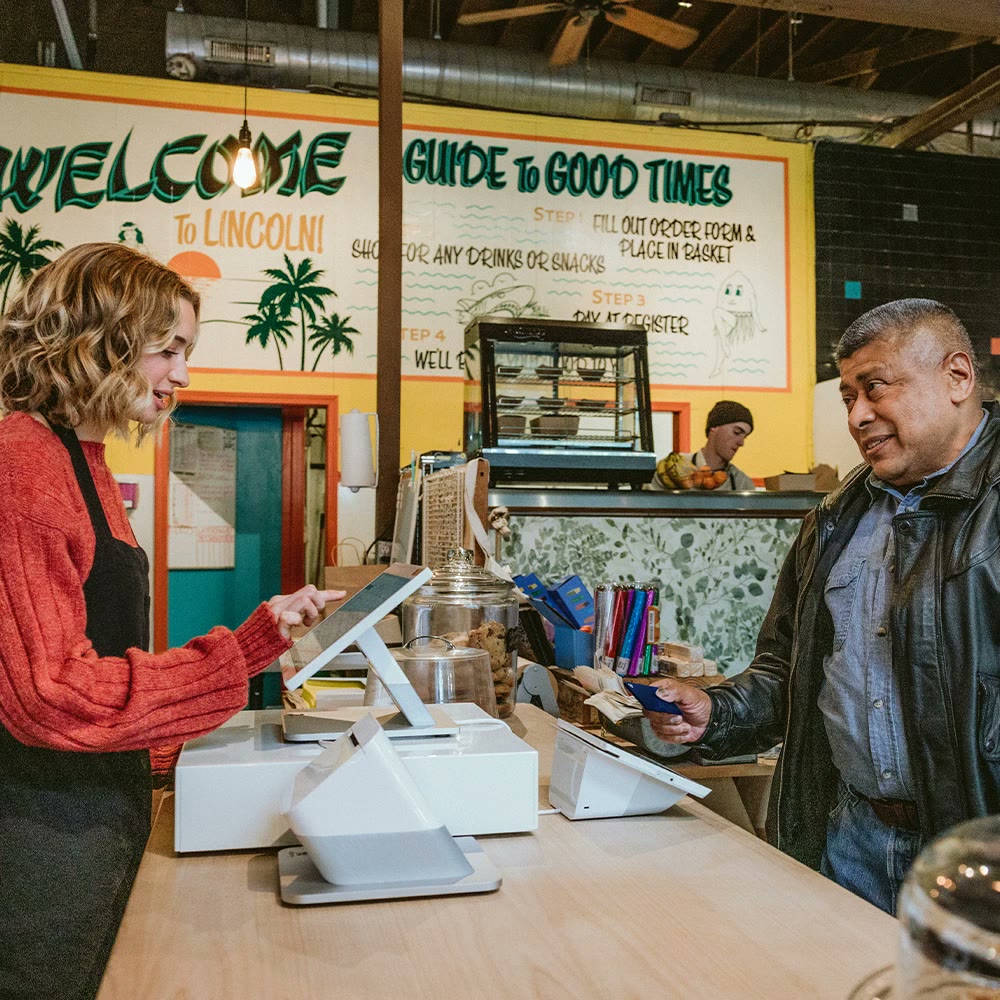 Shop clerk ringing up a smiling customer who is holding a card.